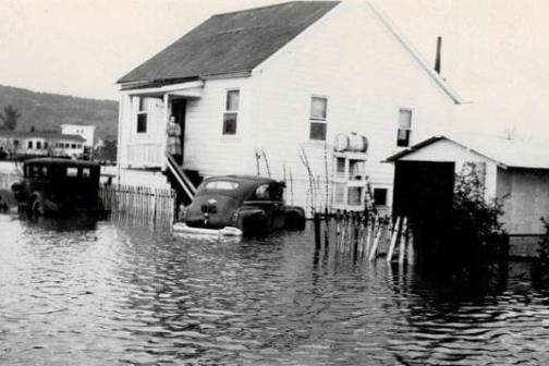 Flooded area with house, cars, and person on steps surrounded by water.